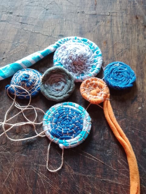 Tiras de tecido enroladas em espiral, em azul, branco e laranja, sobre uma mesa de madeira.
